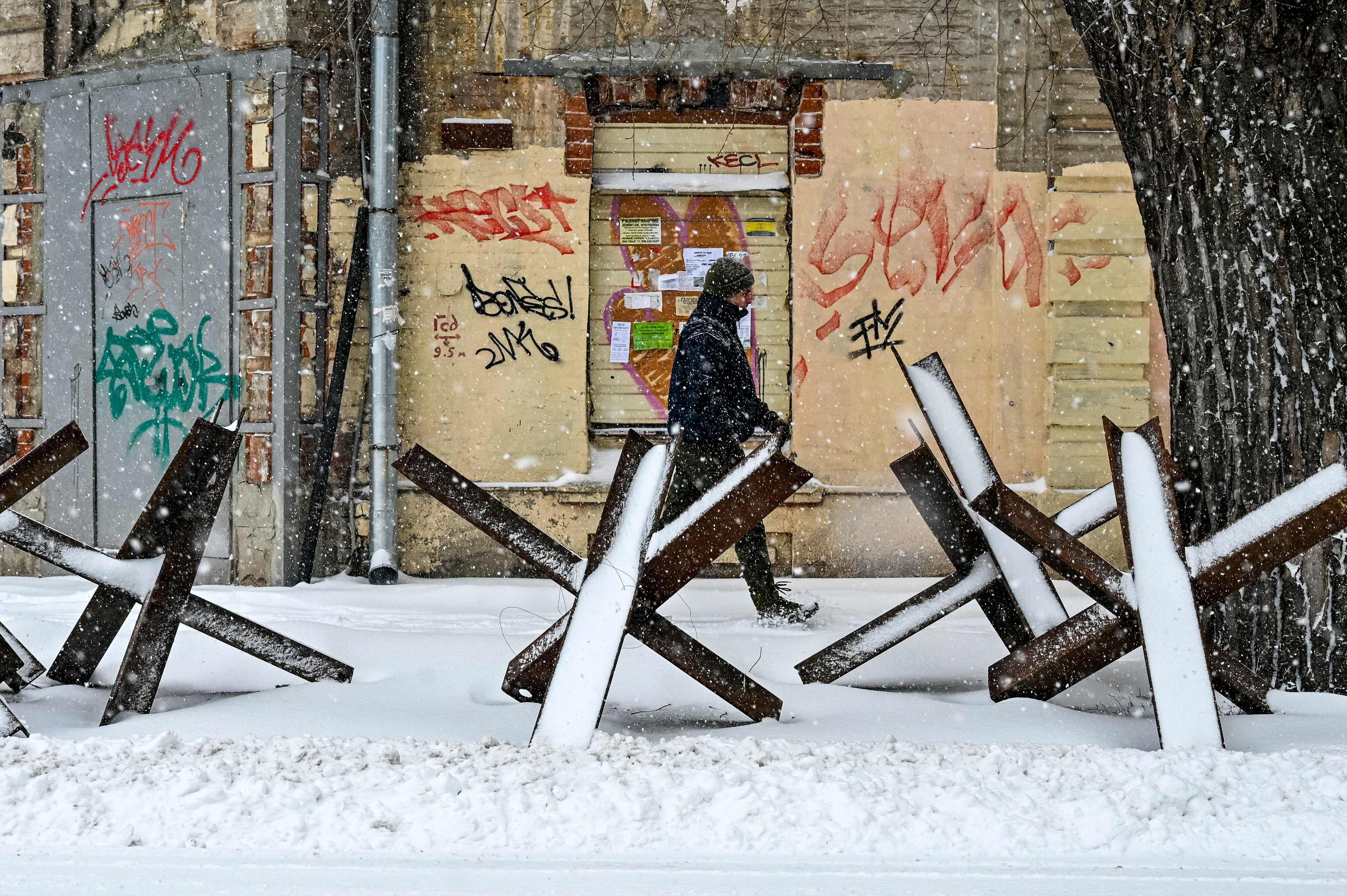 Un hombre camina a través de una calle cubierta por la nieve en la ciudad de Kharkiv, en Ucrania, la cual se encuentra flanqueada por erizos antitanques.