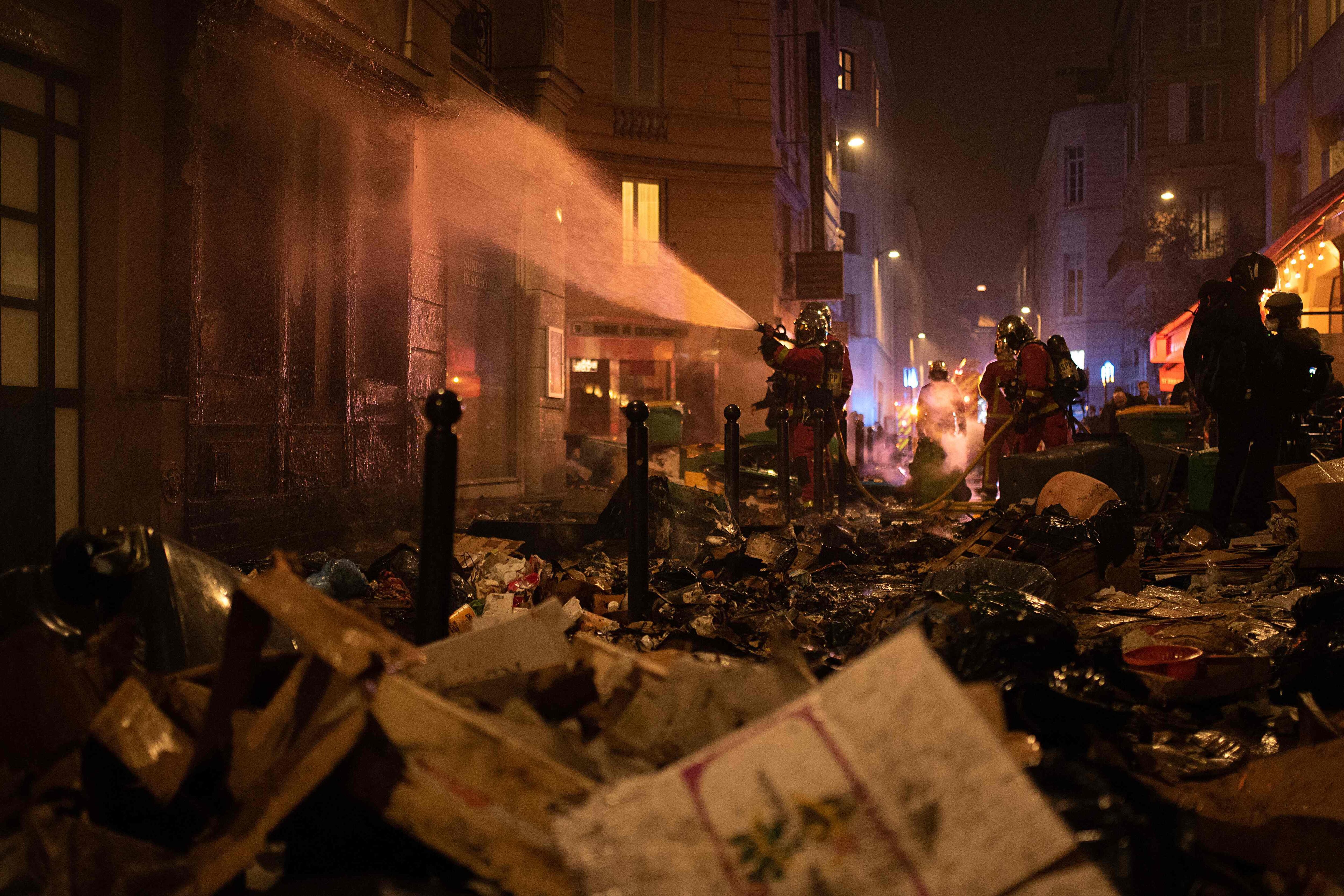 Los bomberos riegan una fachada tras extinguir un fuego de basura durante una manifestación, una semana después de que el gobierno aprobara sin votación en el parlamento una reforma de las pensiones. 