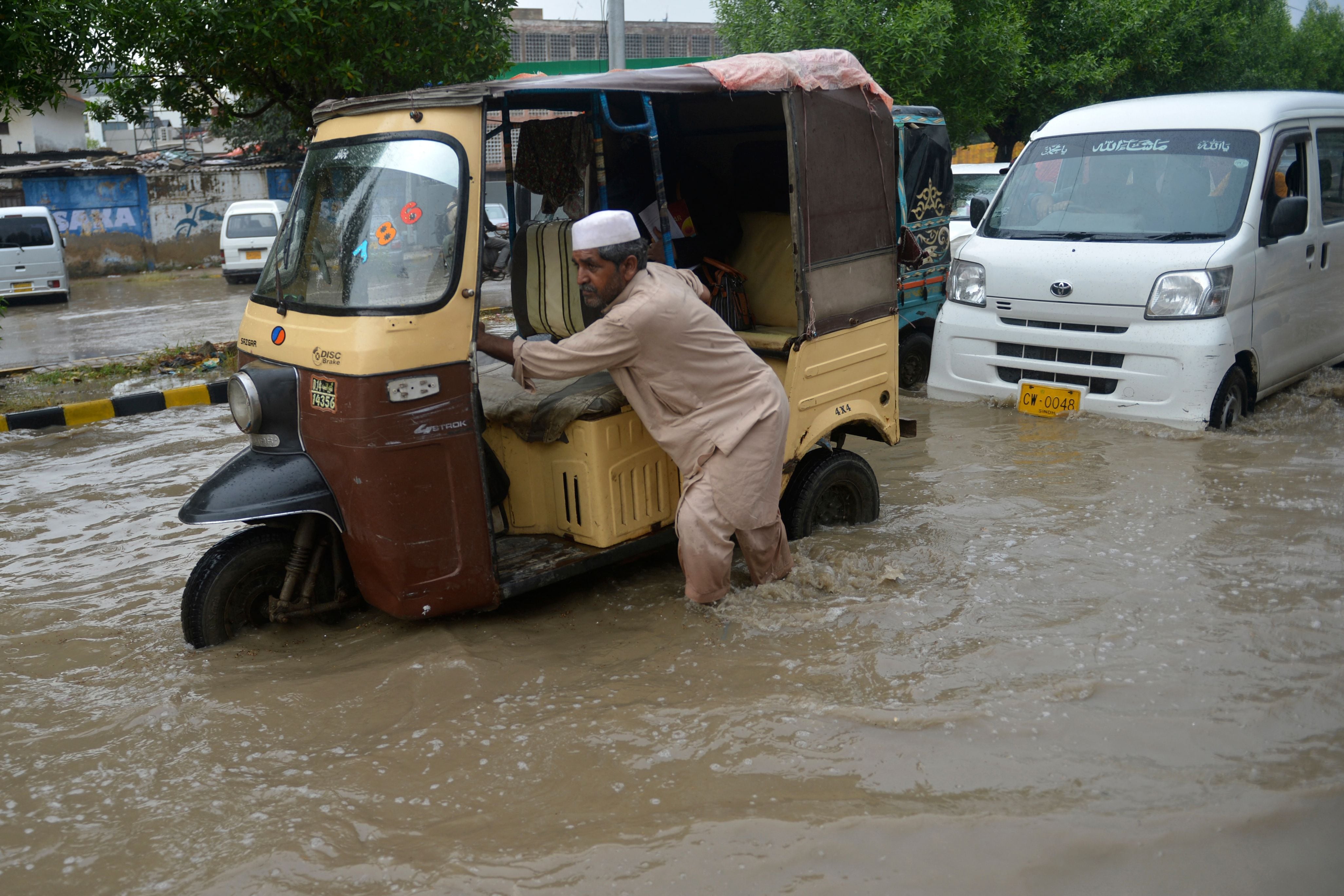 Un hombre empuja su 'tuk-tuk' por una calle inundada después de fuertes lluvias en Karachi, Pakistán, el 13 de septiembre de 2022. (Foto de Rizwan TABASSUM / AFP)