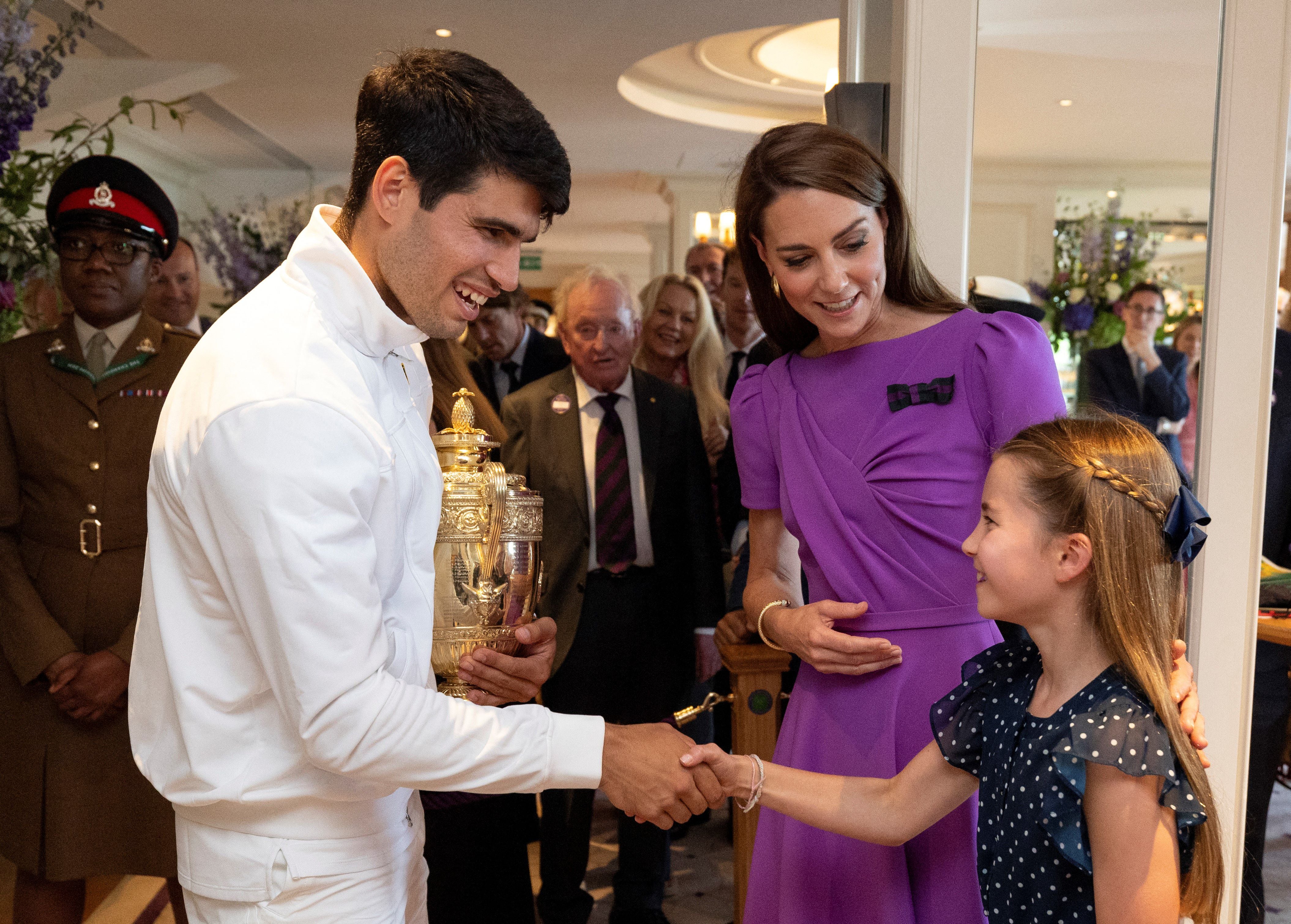 El español Carlos Alcaraz (izq.), sosteniendo el trofeo del ganador, le da la mano a la princesa británica Carlota de Gales (derecha) junto a la británica Catalina, princesa de Gales (centro).