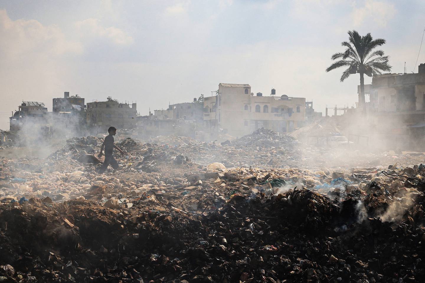 Un joven palestino camina entre montones de desechos humeantes, mientras la recolección de basura y otros servicios municipales se detienen debido al bombardeo israelí de la Franja de Gaza, en el campo de refugiados palestinos de al-Maghazi, en el centro de la Franja de Gaza.