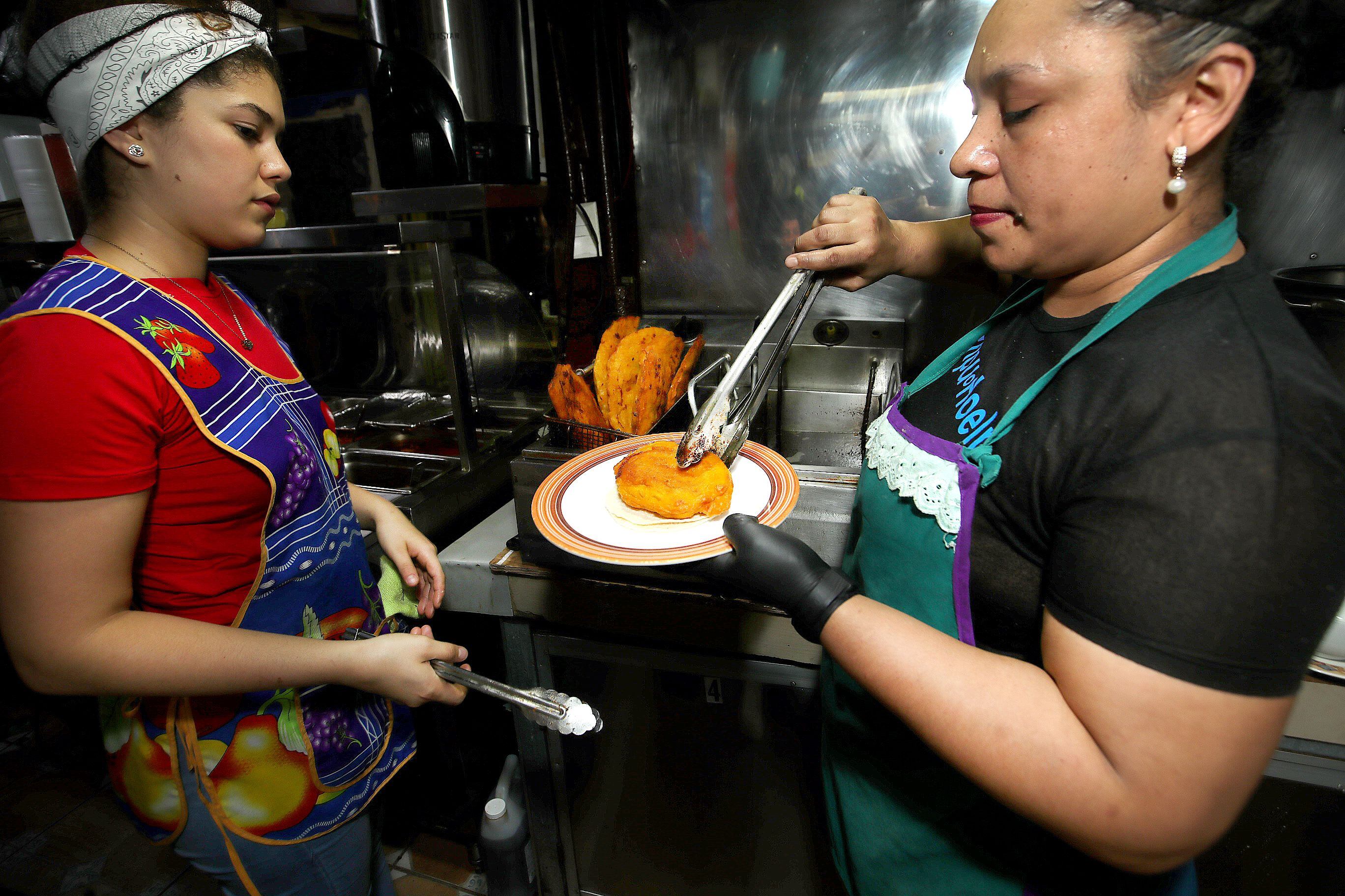La cocinera Meylin Guzmán le entrega el raviol recién salido de la freidora a  Eliana Martinez, encargada de ponerle el repollo, las salsas y tortillas.  Algunos comensales prefieren comerlo solito. 