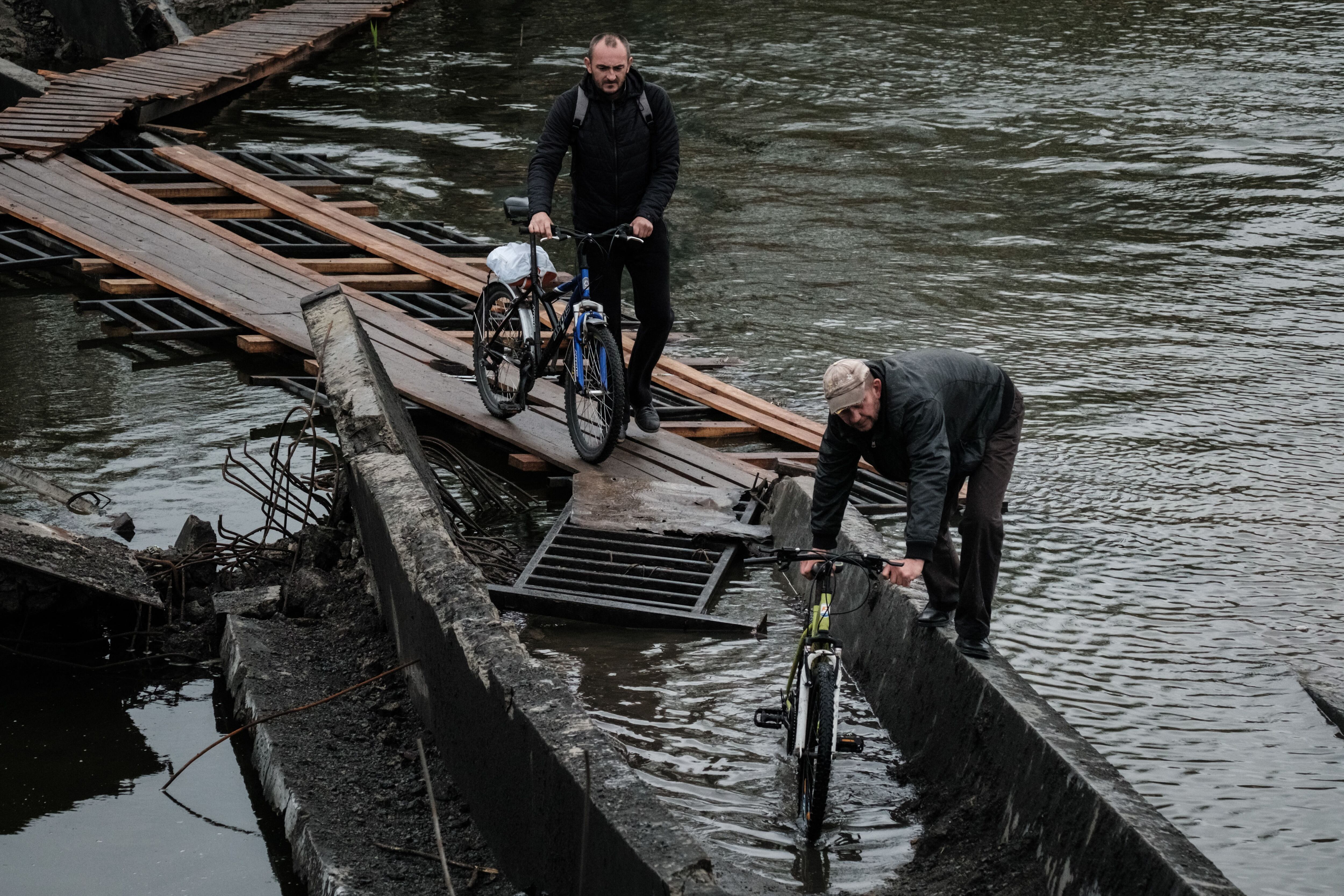 Dos hombres cruzan el puente destruido con sus bicicletas en la ciudad de primera línea de Bajmut, en la región de Donetsk.