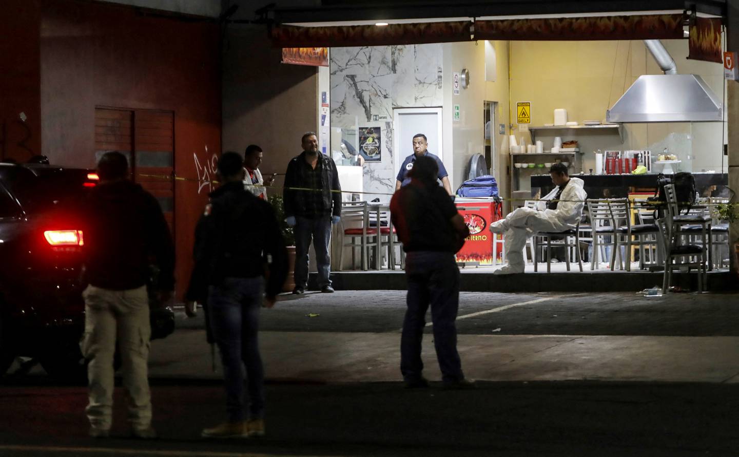 Personal forense e investigadores de la fiscalía son custodiados por policías mientras realizan investigaciones en un restaurante de comida típica mexicana donde fue asesinado Guillermo Torres, presidente municipal de Churumuco.