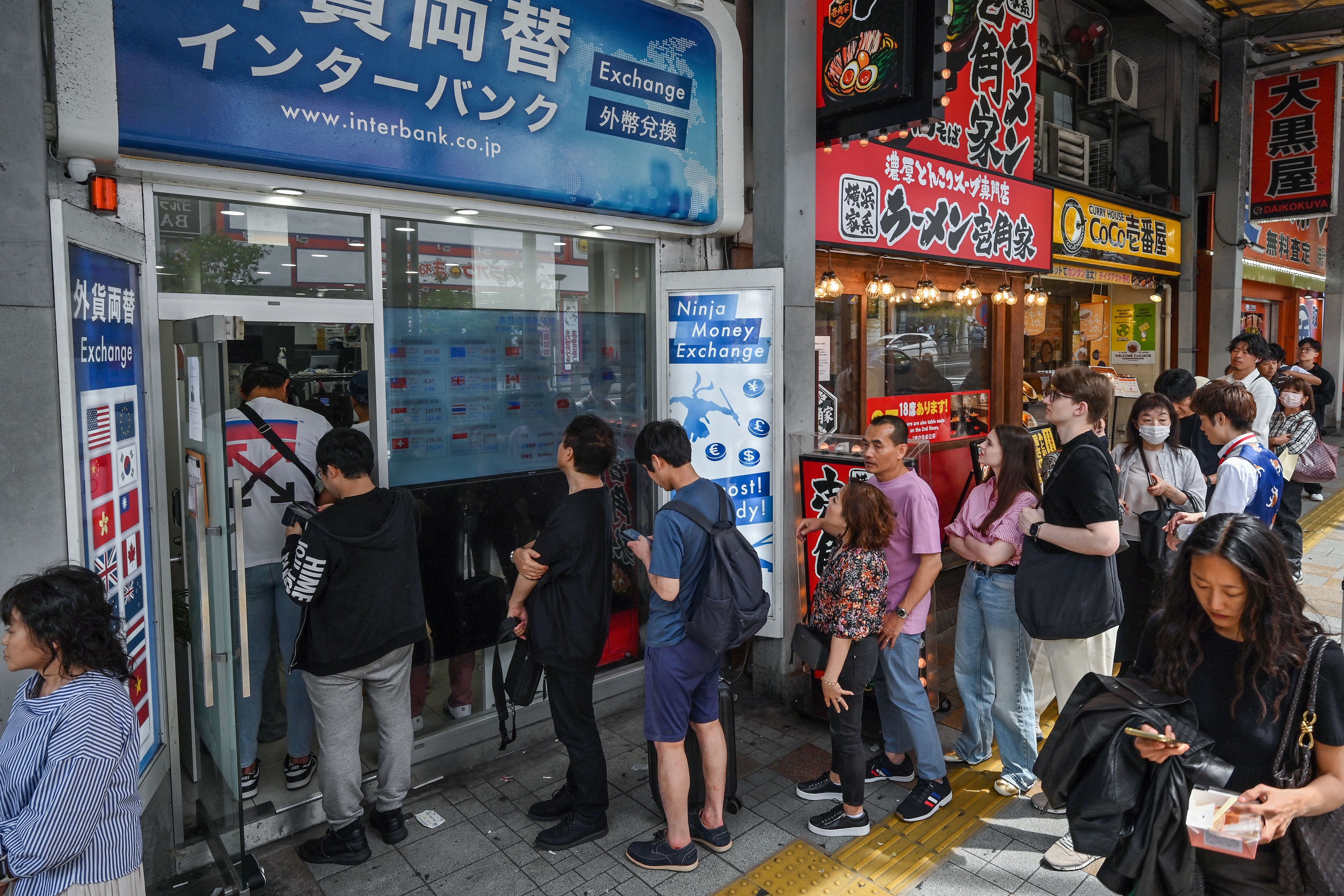 Un grupo de personas hacen fila afuera de una casa de cambio mientras la gente espera para comprar y vender el yen japonés contra moneda extranjera, a lo largo de una calle en el centro de Tokio. Fotografía: