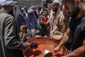Varias personas, sobre todo mujeres y niños, tratan de alimentarse en una conina pública en Deir el Balah, Gaza. Foto: AFP